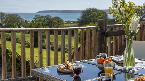 Une table de petit-déjeuner avec des croissants, du jus de fruits et des verres à vin, offrant une vue magnifique sur la mer et la verdure environnante.