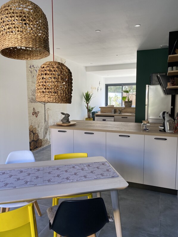 A modern kitchen with a central island, white cabinets, and a dining area with a table and chairs. - Sun Pines (Hourtin)