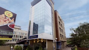 A modern building with a glass facade, a sign for 'FABHOTELS' at the ground level, and a large billboard advertising a lunch buffet. - Fabhotel Arya Regency Hinjewadi (Paud)