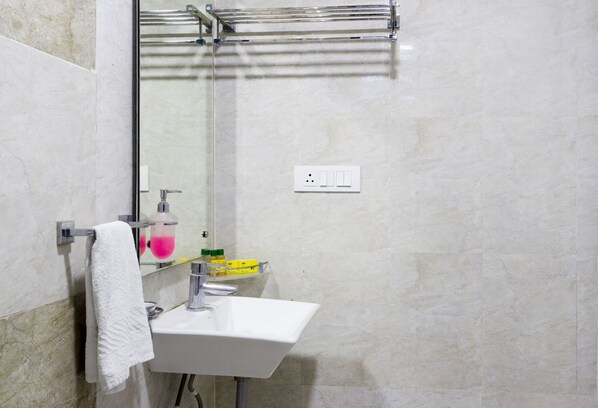 A bathroom with a white sink, a towel hanging on a rack, a mirror, and a shower area. - Fabhotel Arya Regency Hinjewadi (Paud)