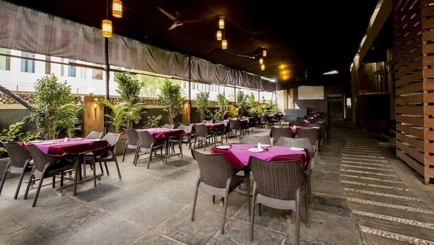 An outdoor restaurant with tables covered in purple tablecloths, wicker chairs, and hanging lantern-style lights. - Fabhotel Arya Regency Hinjewadi (Paud)