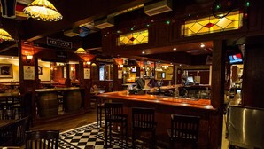 Zona de bar con suelo a cuadros, mostrador de madera y taburetes.