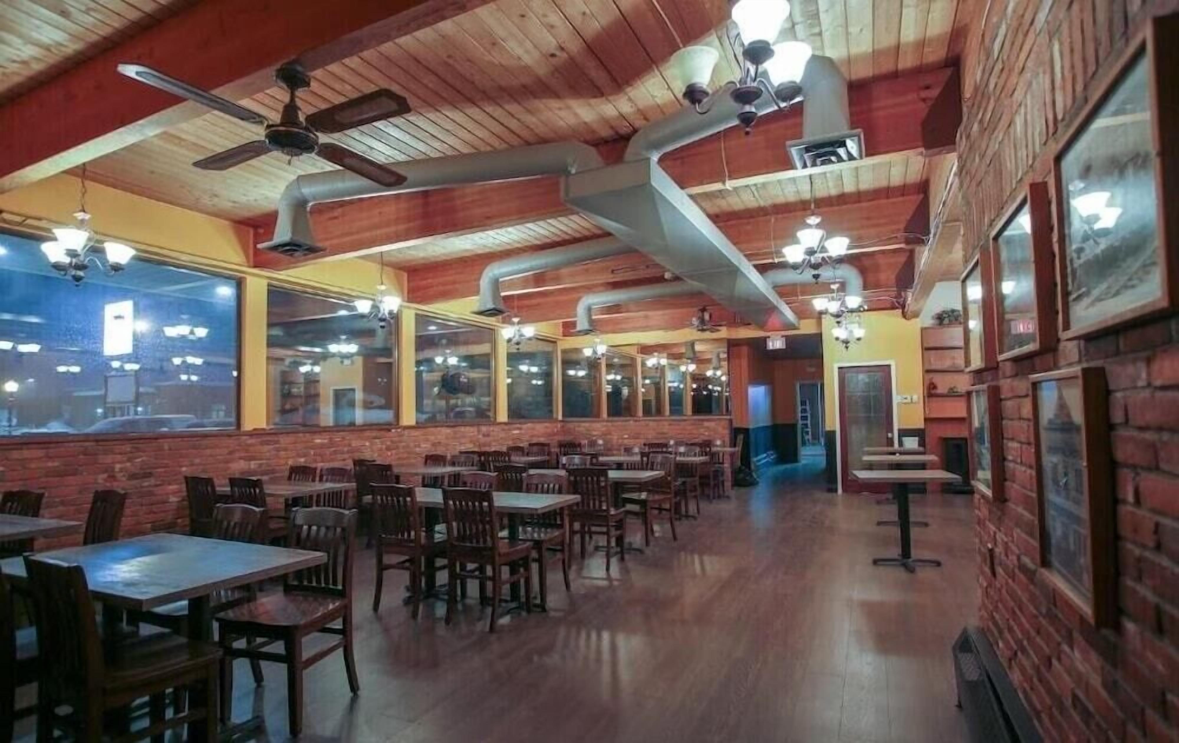 A restaurant with wooden ceilings, multiple ceiling fans, and large windows. Tables and chairs are arranged for dining.