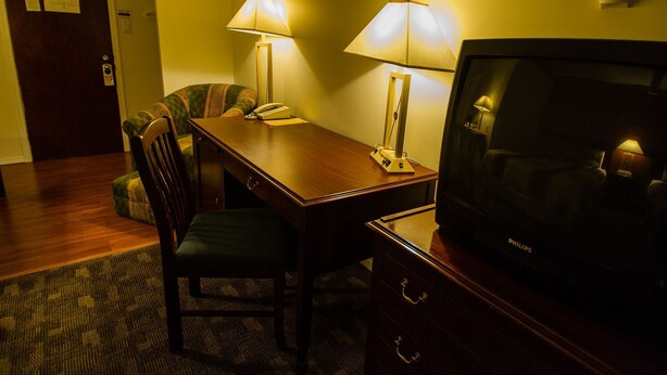 Habitación de hotel con un escritorio de madera, dos lámparas, un televisor, una silla y piso alfombrado.