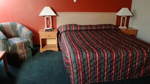 Una habitación de hotel con una cama, una silla, dos mesitas de noche y dos lámparas.