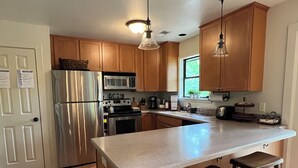 A kitchen with wooden cabinets, stainless steel appliances, a large island with stools, and pendant lighting.