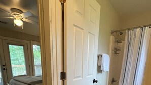 A bedroom with a bed, a bathroom with a shower, and a door leading to another room.