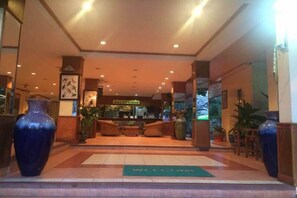 Un hall d’hôtel avec un comptoir d’accueil, de grands vases et un paillasson.