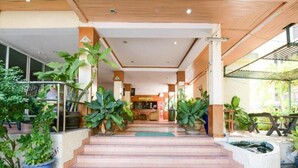Entrada de hotel con una escalera que conduce a una recepción, rodeada de plantas en macetas.