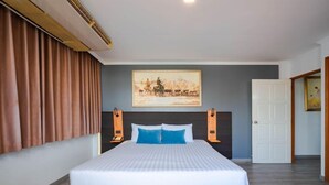 Habitación de hotel con una cama grande, cabecera con decoración de pared, una puerta y una ventana con cortinas.