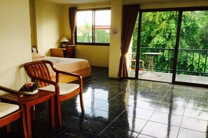 Une chambre d’hôtel avec un lit, une chaise en bois, une petite table et un balcon donnant sur un paysage verdoyant.