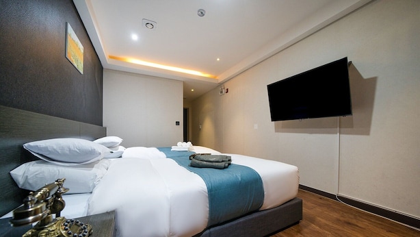 Una habitación de hotel moderna con una cama grande, un televisor de pantalla plana en la pared y suelo de madera.