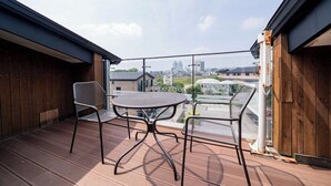Un balcón con mesa y sillas, una valla de madera y vistas a la ciudad.