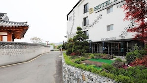 Un edificio de estilo tradicional coreano con un letrero moderno de hotel, un muro de piedra y un área ajardinada.