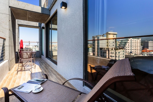 A balcony with a table and chairs, a red umbrella, and a view of the cityscape.