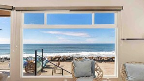 A room with a large window overlooking a beach, wicker chairs, and a small table. - Guest Favorite! Fire Ring on Sand Walk to Village (Oceanside)