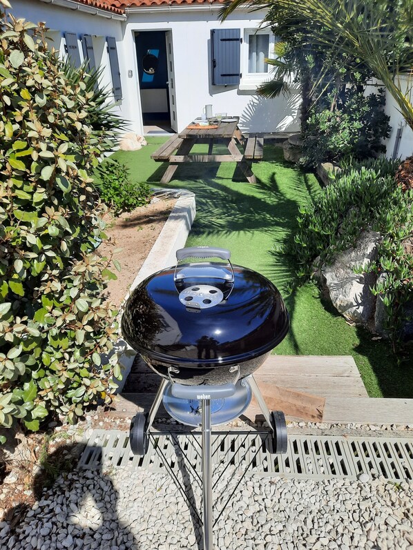 A Weber grill in a backyard with a patio, a white house, and green landscaping. - House with patio 5 minutes from the beach (L'Épine)