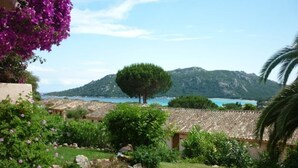 A garden with a lawn, a tree, and a view of a mountain and sea. - Villa Tout Confort 400 m de la Plage (Porto-Vecchio)