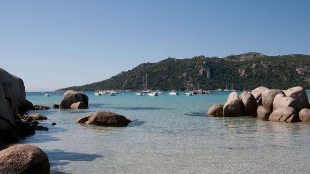A coastal scene with large rocks in shallow water, clear turquoise sea, boats, and a hilly background. - Villa Tout Confort 400 m de la Plage (Porto-Vecchio)