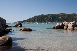 A coastal scene with large rocks in shallow water, clear turquoise sea, boats, and a hilly background. - Villa Tout Confort 400 m de la Plage (Porto-Vecchio)