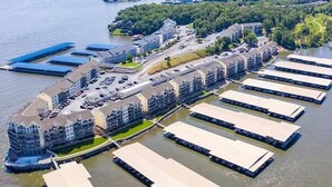 Vista aérea de uma propriedade à beira-mar com várias embarcações atracadas, um estacionamento e um edifício grande com vários andares.
