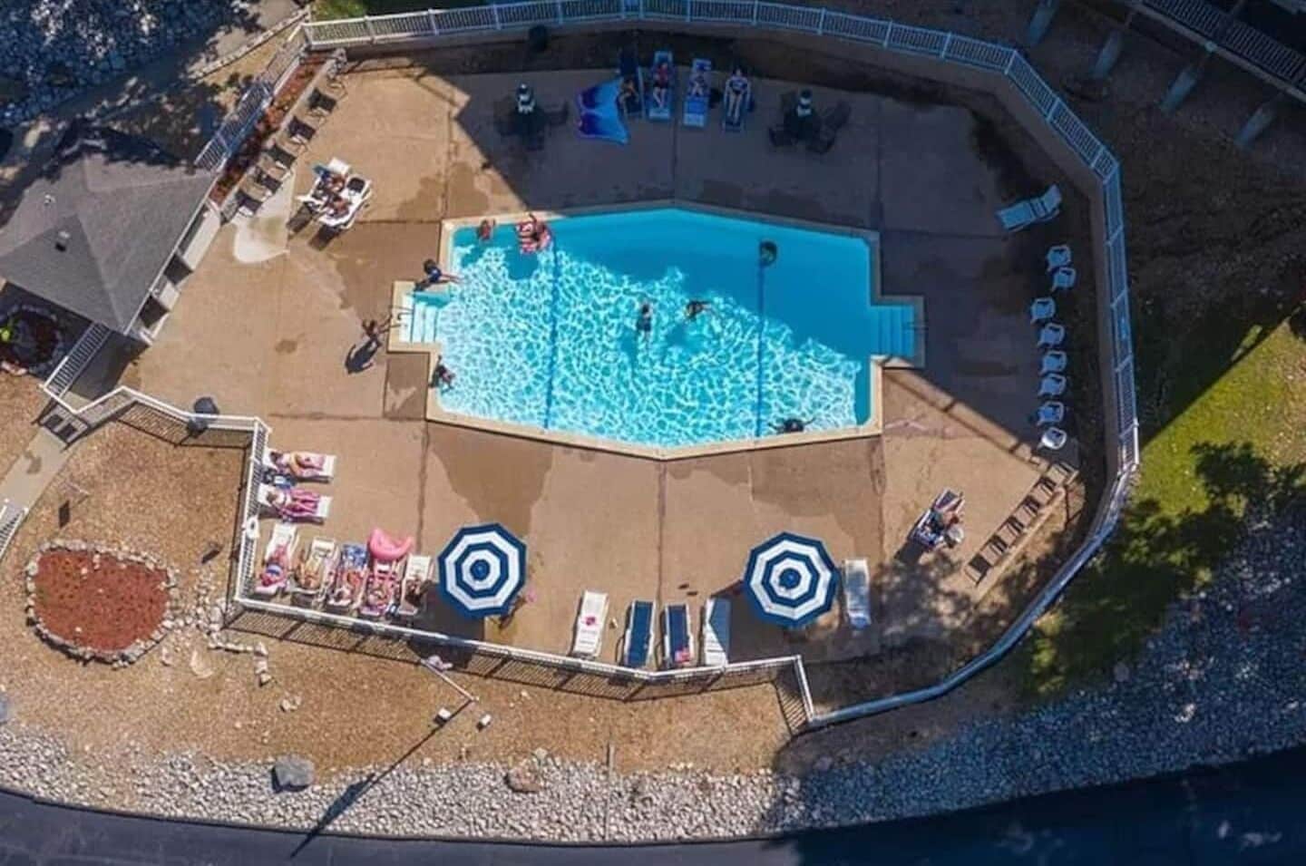 An aerial view of a swimming pool area with a pool, sun loungers, umbrellas, and a small garden area.