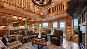 A spacious log cabin interior with a large dining area, multiple seating options, and large windows offering scenic views. - Cherokee Vista - Pet Friendly | Mountain Views | Hot Tub | Shuffleboard | Fire Pit (Blue Ridge)