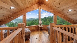 A wooden interior with a large window offering a view of a forested landscape. - Cherokee Vista - Pet Friendly | Mountain Views | Hot Tub | Shuffleboard | Fire Pit (Blue Ridge)