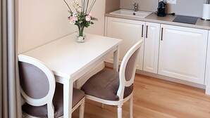 Une petite cuisine moderne avec des meubles blancs, un plan de travail blanc et un évier noir. On y trouve une petite table avec deux chaises et un vase de fleurs.