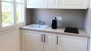 Une cuisine avec des meubles blancs, un évier et une bouilloire noire posée sur le plan de travail.
