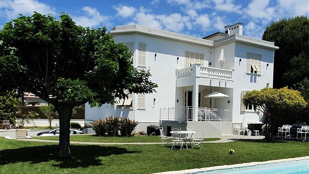 Un bâtiment blanc doté d’une piscine, entouré de pelouse et d’arbres.