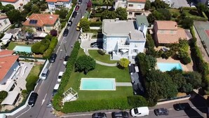 Vue aérienne d’un quartier résidentiel avec une grande maison dotée d’une piscine, d’un court de tennis et d’une pelouse bien entretenue.