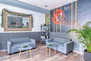 Un hall moderno con dos sofás grises, un mural con temática de café, un espejo decorativo y una estantería.