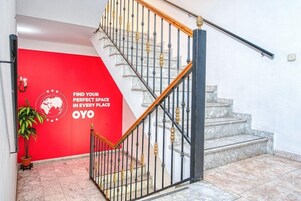 Una escalera con pared roja que muestra un logotipo y texto, escalones de mármol y una planta en maceta.