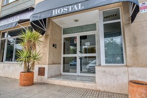 Un edificio con un letrero que dice "HOSTAL" sobre la entrada, una planta en maceta al frente y un coche estacionado afuera.