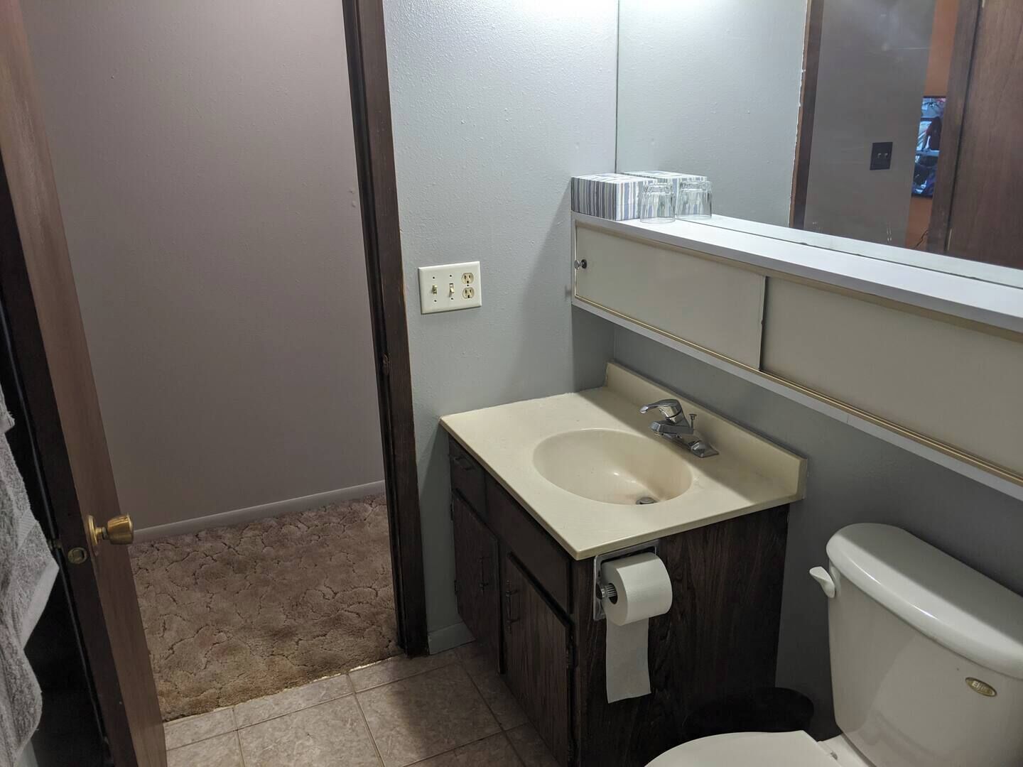 Un baño con lavamanos blanco, un espejo y un inodoro. Hay una toalla colgada en la puerta.