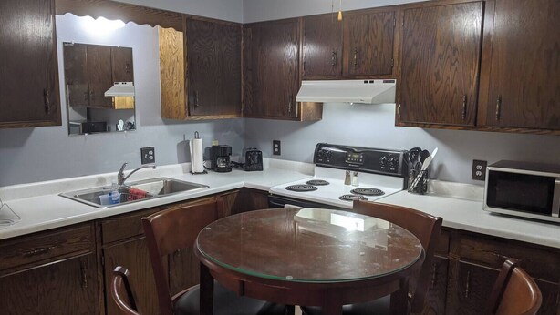 A compact kitchen with dark wooden cabinets, a white countertop, a round glass table, and black chairs. - Wonderfully located two bedroom apartment (Pierre)