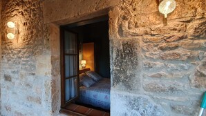 A stone-walled room with a bed, a window, and a wall-mounted light fixture. - A house of character (Puy-l'Évêque)