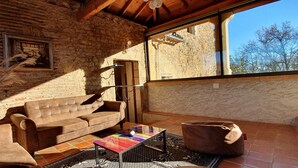 A cozy room with a stone wall, a wooden ceiling, a sofa, a coffee table, and a window with a view of trees. - A house of character (Puy-l'Évêque)