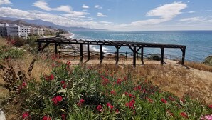Blick auf die Küste mit einer Holzpergola, einem Strand und Gebäuden im Hintergrund.
