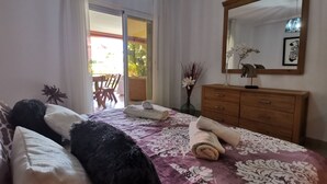 Ein Schlafzimmer mit Bett, einem Holzschrank, einem Spiegel und Blick auf einen Balkon.