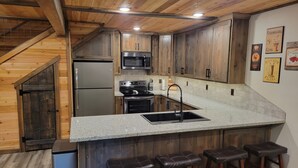 A kitchen with wooden cabinets, stainless steel appliances, a granite countertop, and a bar area with stools.