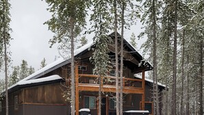 A wooden cabin with a large porch, surrounded by tall trees and covered in snow.