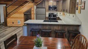 A modern kitchen with wooden accents, a central island, bar stools, and a dining table with a potted plant.