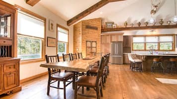 Un grand espace à manger avec une longue table en bois et des chaises, une cuisine équipée d’appareils modernes et un mur en pierre rustique portant l’inscription « L’endroit où l’on se retrouve ».