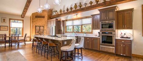 Una cocina amplia con suelos de madera, una isla central, taburetes de bar y electrodomésticos modernos.