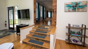 A spacious living room with a wooden staircase, a flat-screen TV, and a bookshelf. - Vista Michigana, Lake Michigan (Riverside)