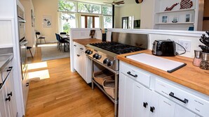 A modern kitchen with a gas stove, oven, and a wooden countertop. There is a dining area with a table and chairs visible in the background. - Vista Michigana, Lake Michigan (Riverside)