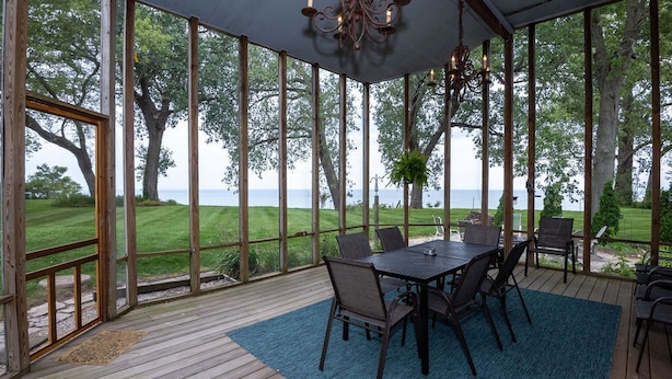 A covered outdoor patio with a table and chairs, overlooking a grassy area and a body of water. - Vista Michigana, Lake Michigan (Riverside)