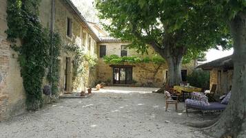 Une cour avec un sol recouvert de gravier, un arbre et un bâtiment doté d’une porte et de fenêtres.